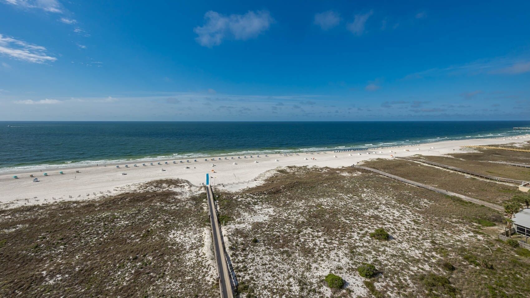 A coastal road leading to a beach with a sandy shoreline and sparse vegetation.