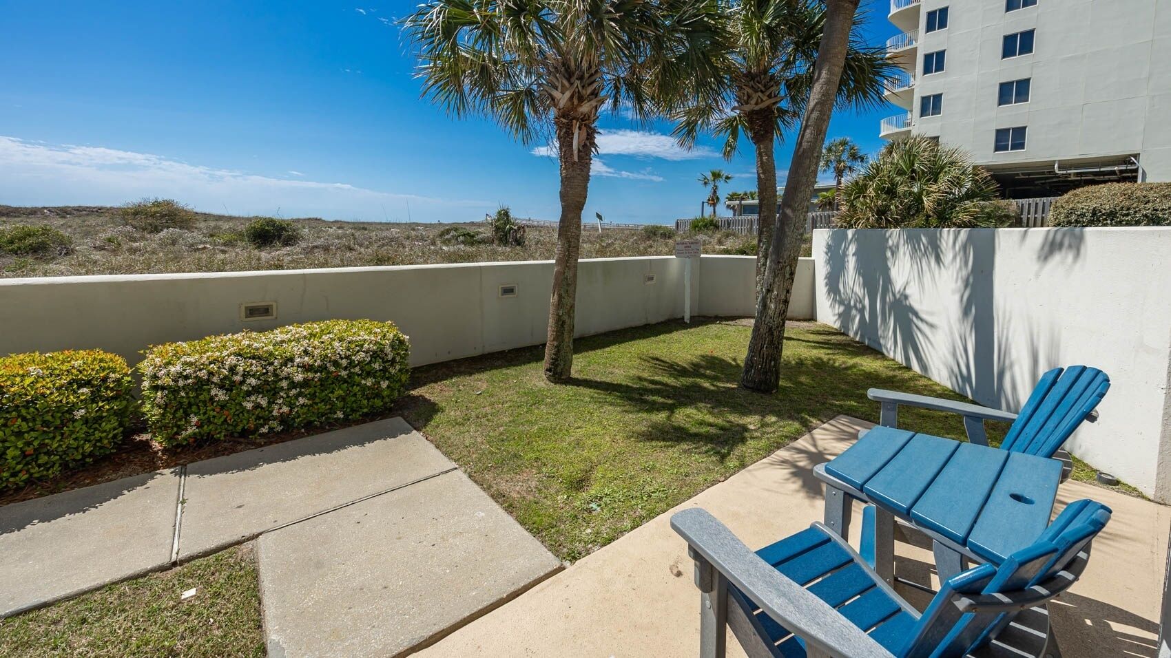 A patio with a table and chairs, a small lawn, and a building in the background.