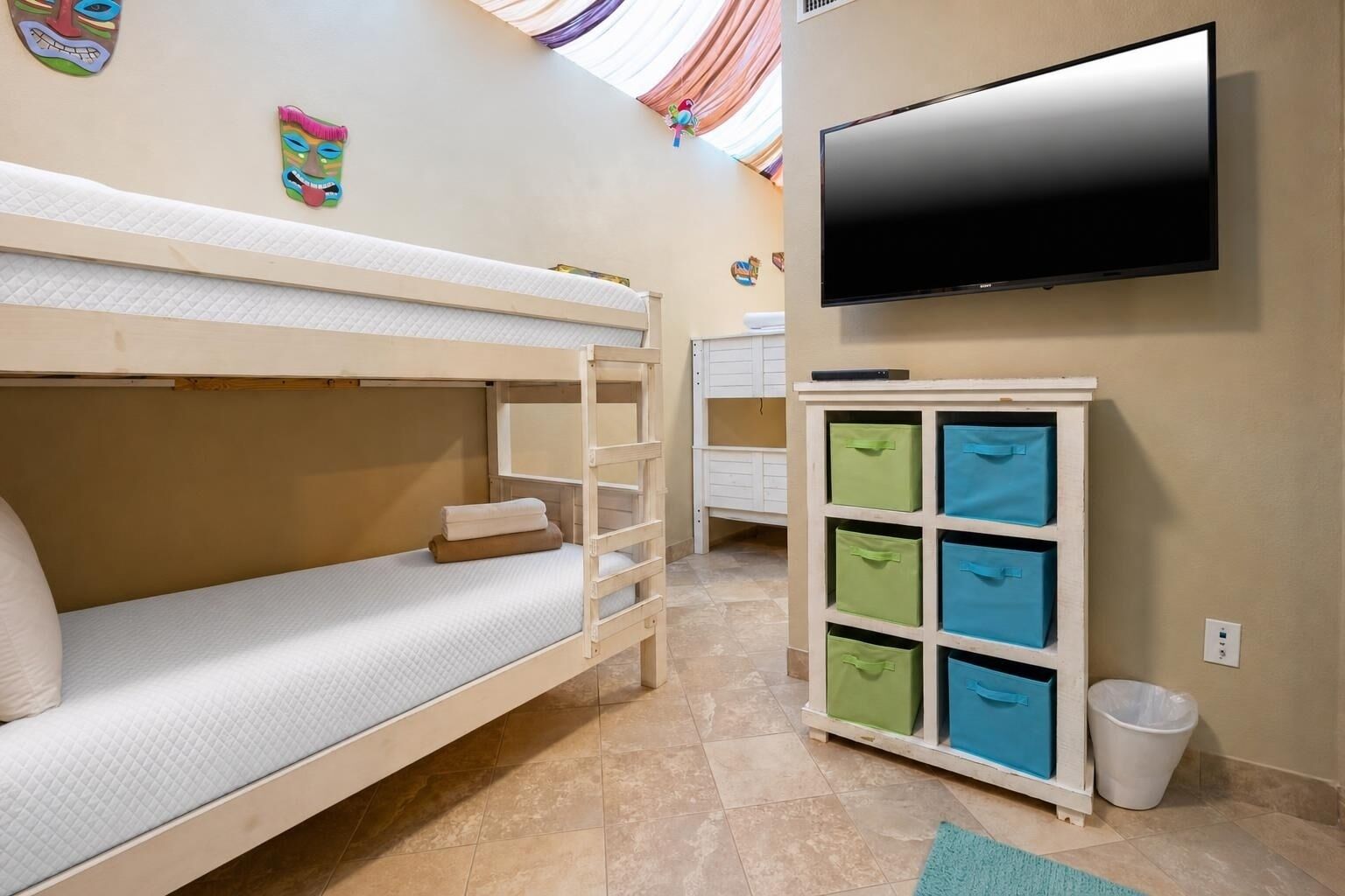 Ein Mehrbettzimmer mit Fernseher, Aufbewahrungsboxen und einem Mülleimer.