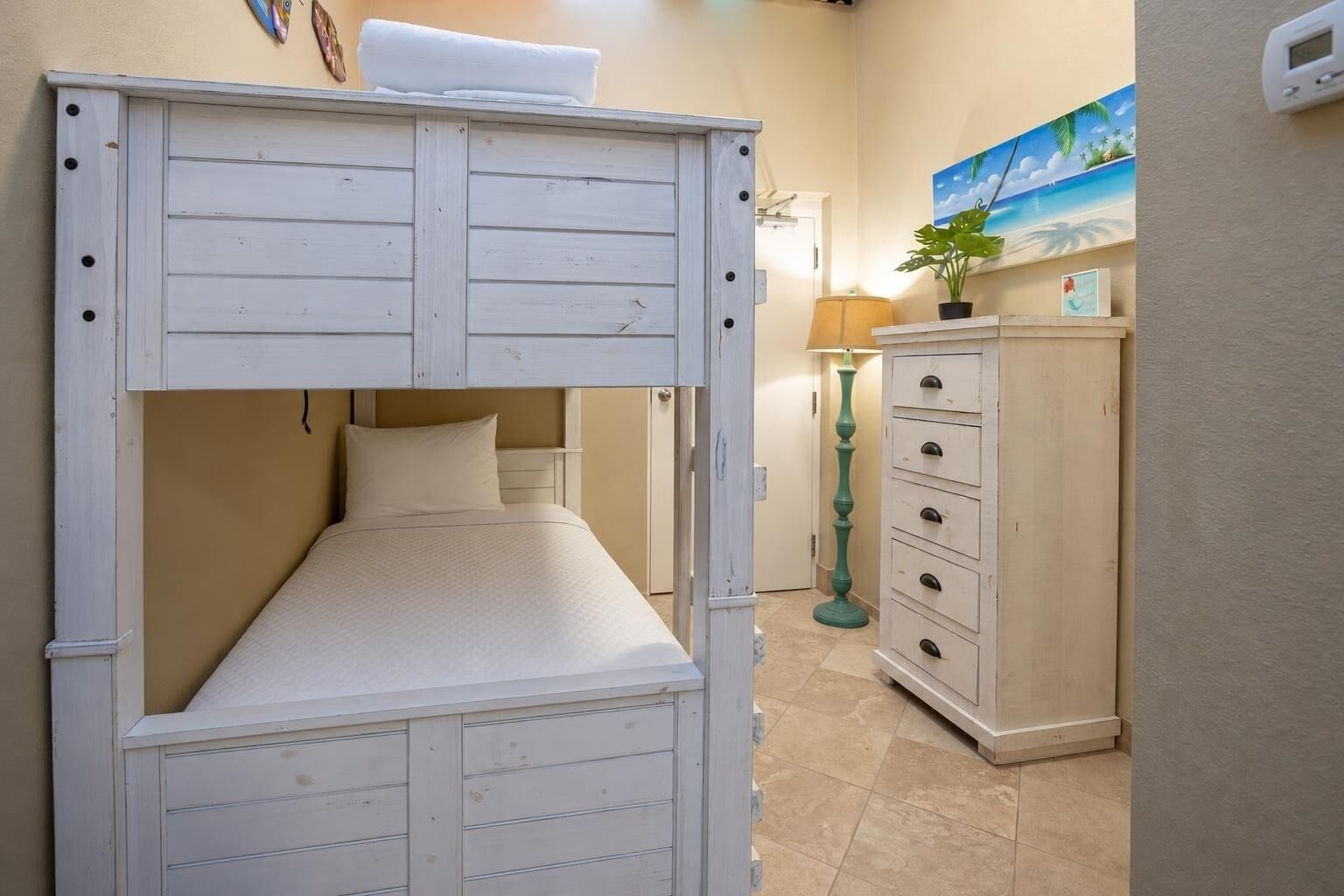 A bunk bed with a small desk and drawers, a lamp, and a painting on the wall.