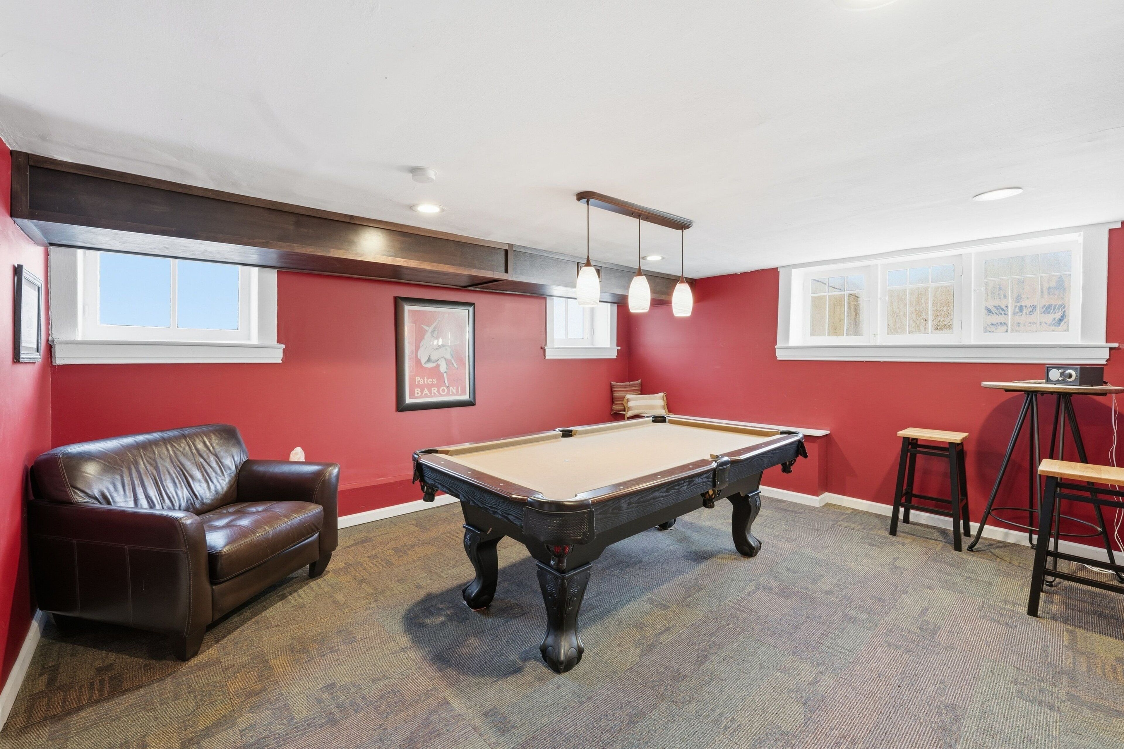 A pool table in a room with red walls, a leather couch, and a bar area.