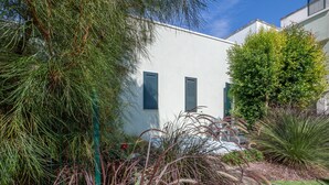 Un bâtiment à l’extérieur blanc et aux volets verts, entouré de différentes plantes et arbres.