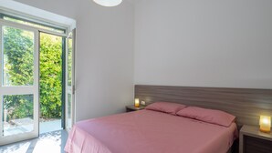 Une chambre avec un lit, une table de chevet, une lampe et une vue sur la verdure, visible à travers une porte vitrée.