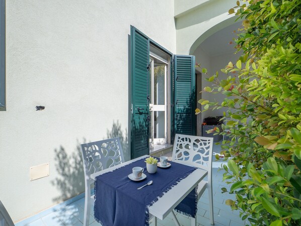 Un espace extérieur aménagé pour prendre les repas, avec une table dressée pour deux personnes, une chaise et un pot de fleurs.
