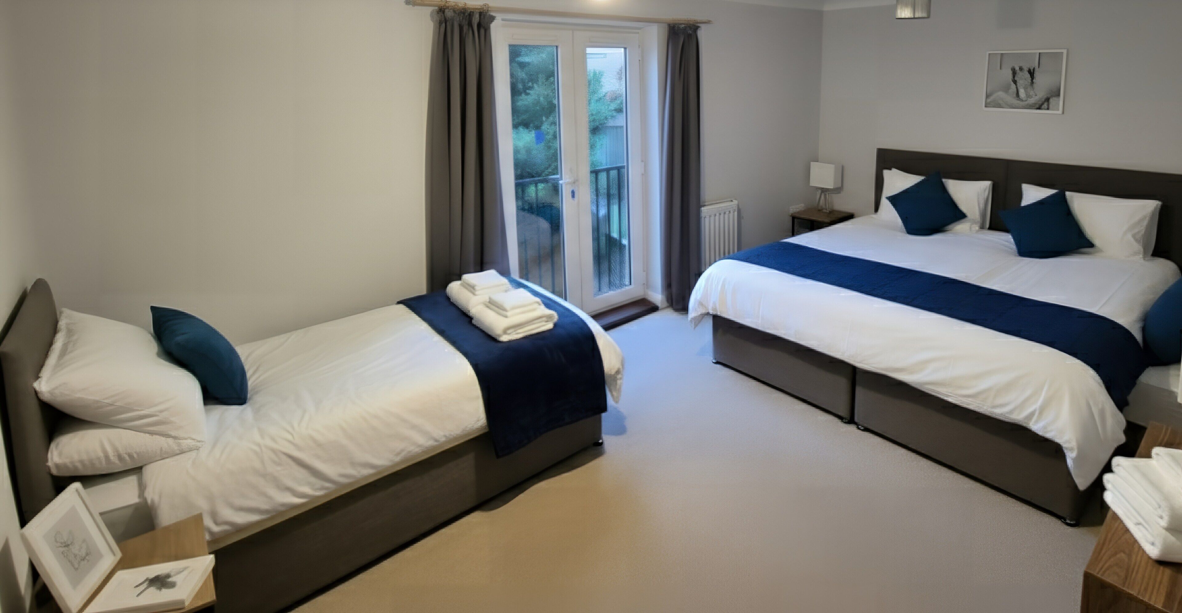 A hotel room with two beds, a window with curtains, a radiator, and a framed picture on the wall.