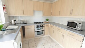 A modern kitchen with light wood cabinets, stainless steel appliances, a gas stove, a toaster, a microwave, and a sink. - Charming 4-bedroom Stoke Gifford Retreat for 9 Guests (Bristol)