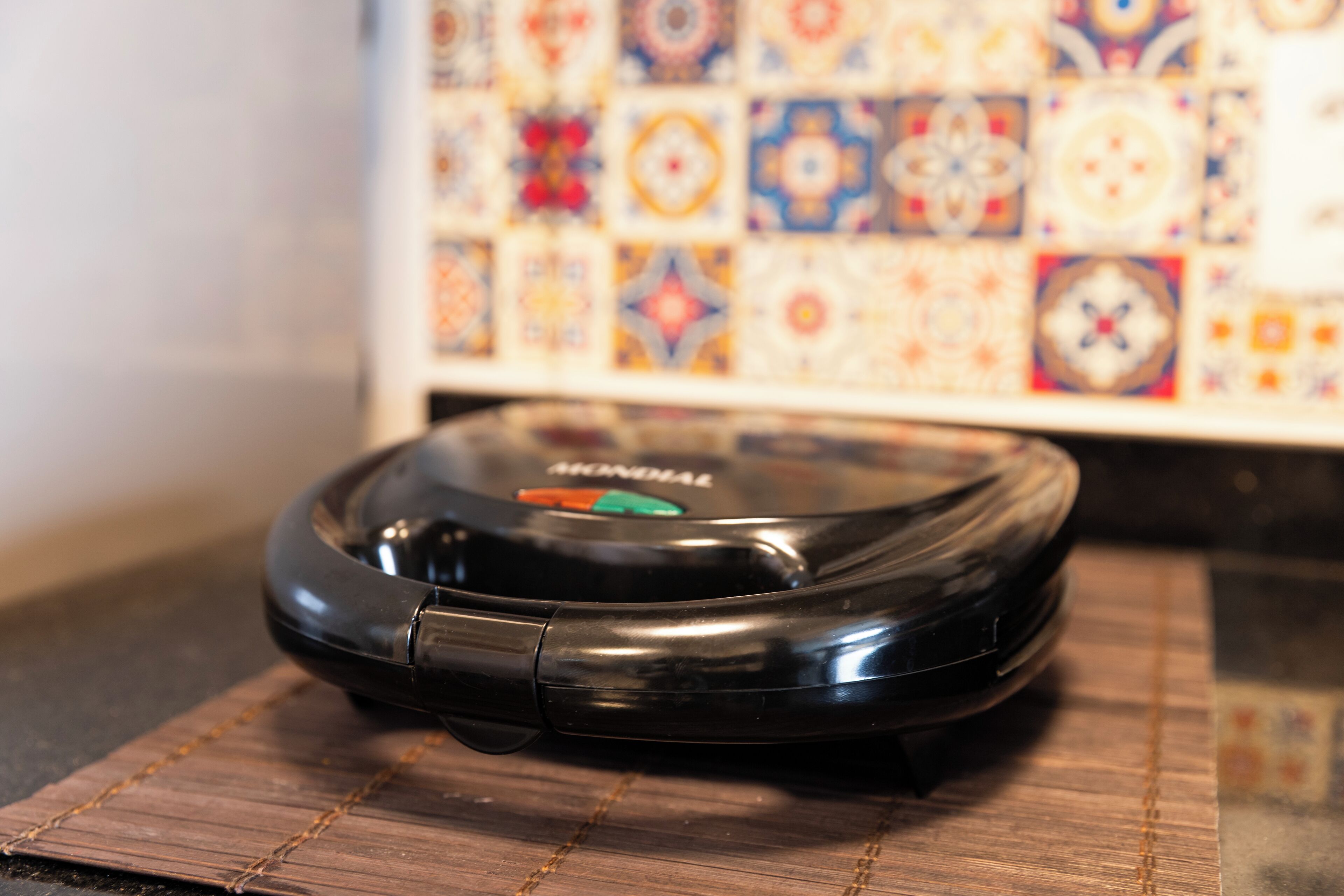 Een zwarte robotstofzuiger op een houten vloer, met een behangetje met patroon op de achtergrond.