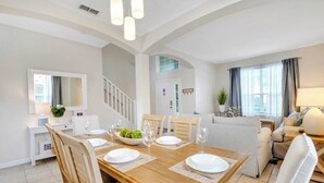 A spacious living room with a wooden dining table set for four, a sofa, and a lamp.