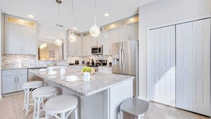 A modern kitchen with white cabinetry, a marble island with bar stools, stainless steel appliances, and pendant lighting.