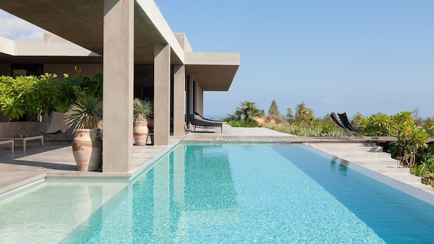A pool area with lounge chairs, potted plants, and a clear view of the ocean.