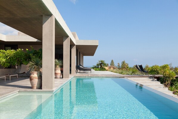 A pool area with lounge chairs, potted plants, and a clear view of the ocean.