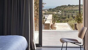 A modern bedroom with a large sliding glass door leading to a balcony with a view of the countryside.