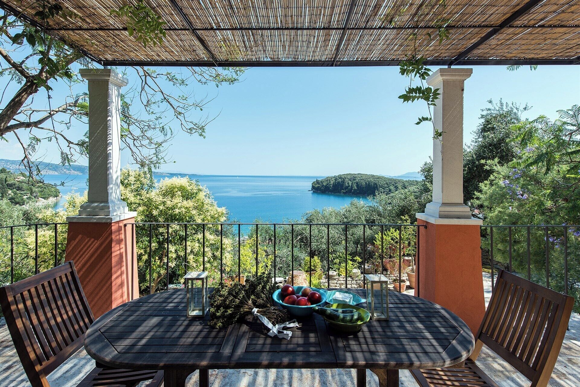 Uma área de refeições ao ar livre com mesa e cadeiras, vista para o mar e uma estrutura de pérgola.