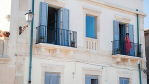 Un edificio con varios balcones, cada uno con barandilla negra y contraventanas azules.