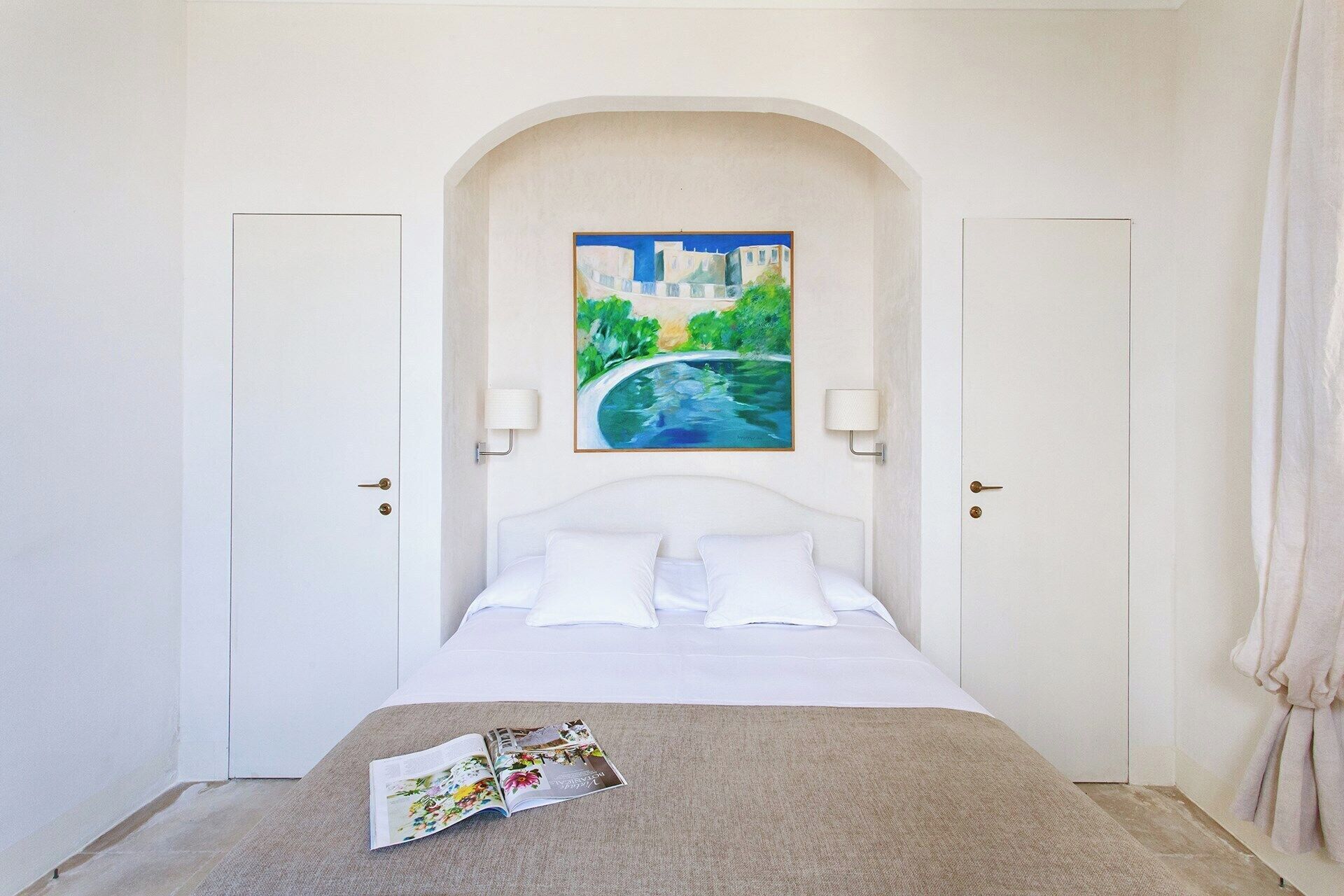 A bedroom with a bed, a painting of a cityscape, and a magazine on the bed.