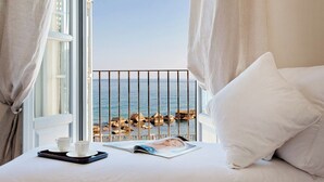 Un dormitorio con vista al mar, una cama con almohadas blancas, una bandeja con taza y platillo, y una revista sobre la cama.