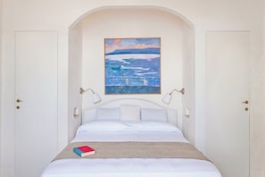 A bedroom with a bed, a painting above the bed, and two doors.