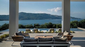 Zona salotto esterna moderna con vista su un lago e montagne.