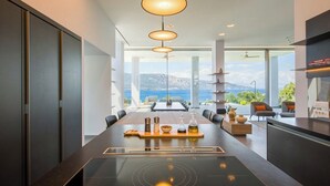 Una cucina moderna con isola centrale, illuminazione a sospensione e vista sul mare.