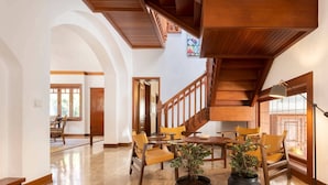 Un salón amplio con techo alto, escalera de madera y un comedor con sillas amarillas.
