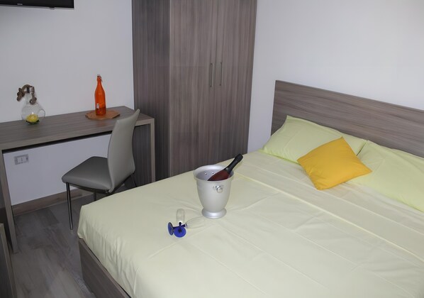 A hotel room with a bed, a desk, a chair, a bottle, and a glass.