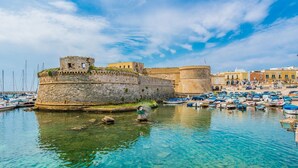 A historic stone fortification with clear blue water in front, surrounded by a marina with boats. - Apartment 'Piccolo' with Shared Garden and Air Conditioning (Porto Cesareo)