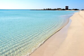 A beach with clear water, a sandy shore, and a distant building.