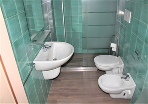 A bathroom with a bidet, toilet, and sink, all with modern fixtures.