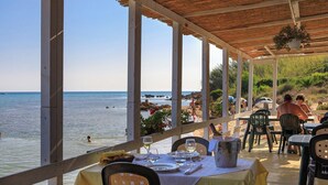 An outdoor dining area with tables set for two, overlooking a beach with people swimming and walking. - Chirchiaro - Four Bedroom Villa, Sleeps 8 (Salemi)