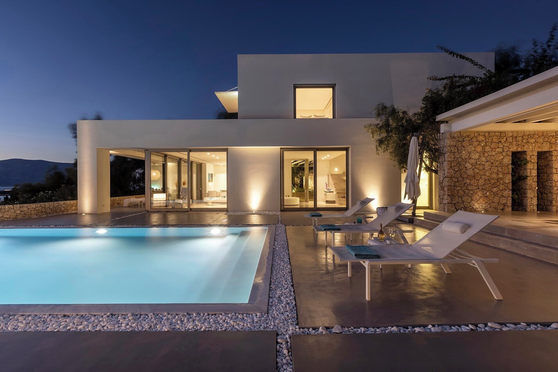 Ett modernt hus med en swimmingpool, utomhusmöbler och en stenmur.
