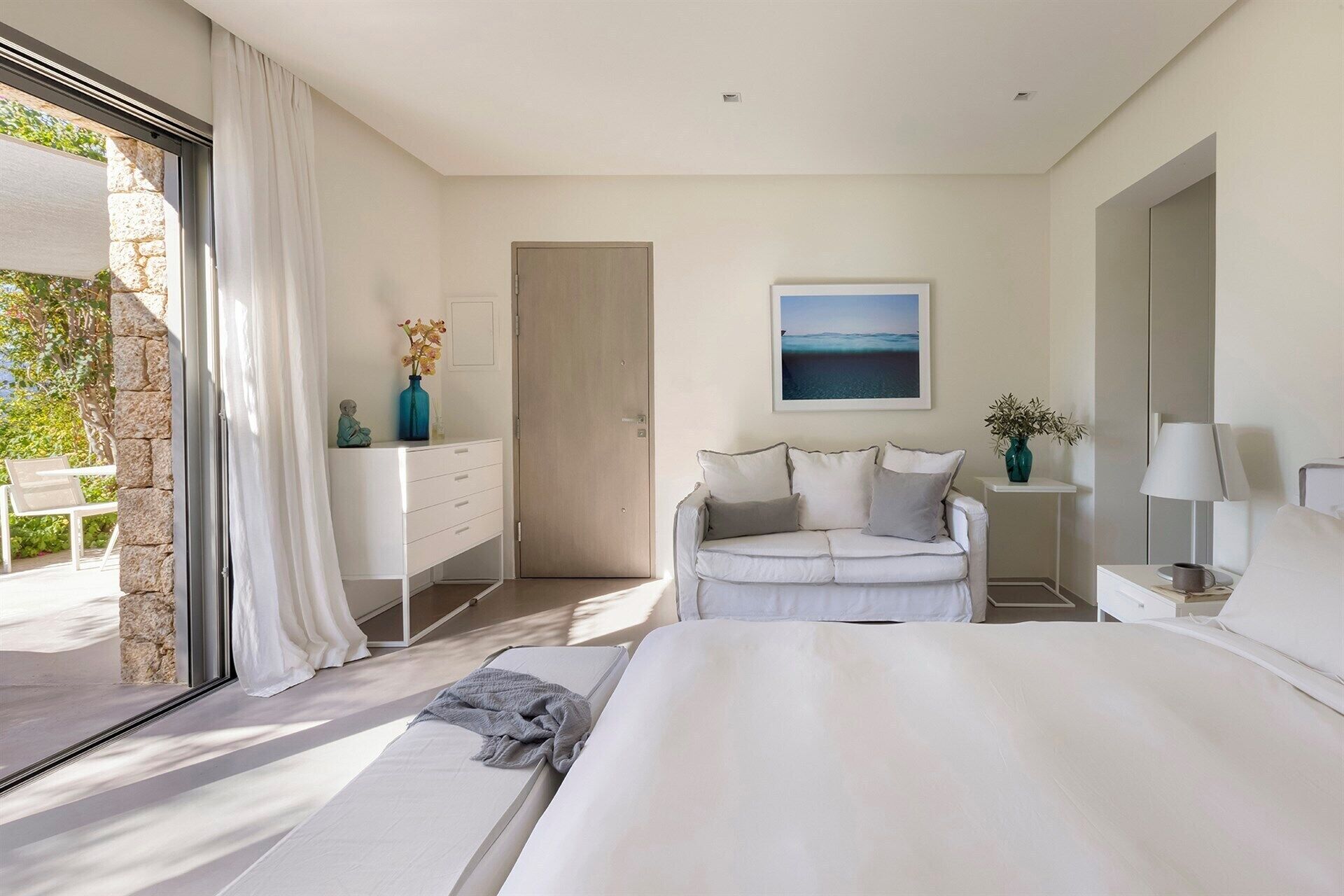 Un dormitorio moderno con una cama grande, un tocador blanco, un sofá y un cuadro en la pared.