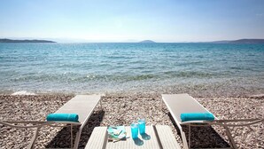 Blick auf einen Strand mit zwei Liegestühlen, einem Handtuch und einer Wasserflasche am Kiesufer.