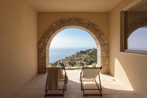 Un balcón con un arco de piedra, dos sillas y vistas al paisaje costero.