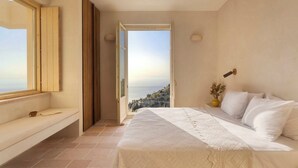 Une chambre à coucher avec un lit, un banc, une table de chevet, une lampe et une vue sur la mer.