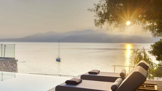 A serene poolside area with lounge chairs and a glass balustrade overlooking a calm body of water and distant mountains. - Eolia - Three Bedroom Villa, Sleeps 6 (Nikiana)