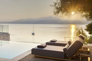 Un'area piscina tranquilla con sedie a sdraio e un parapetto in vetro che si affaccia su un'acqua calma e montagne in lontananza.