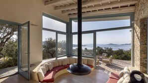 A modern interior with a circular seating area, large windows offering a view of the sea, and a stone wall.