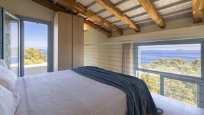 A bedroom with a large bed, wooden ceiling beams, and a view of the sea.