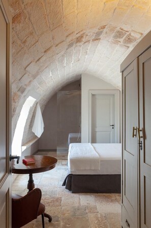 A bedroom with a stone ceiling, a bed, a small table with a book, and a chair. - Masseria Donnagnora - Five Bedroom Villa, Sleeps 10 (Ostuni)