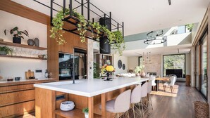 A modern kitchen with a central island, wooden cabinetry, and a hanging plant arrangement.