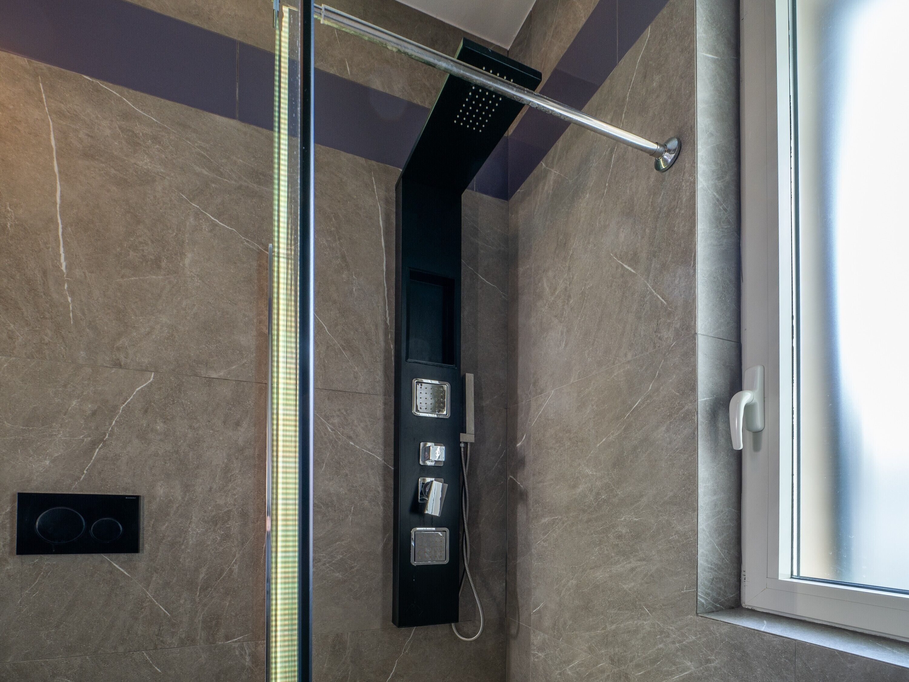 A modern bathroom with a glass-enclosed shower, a control panel, and a window.