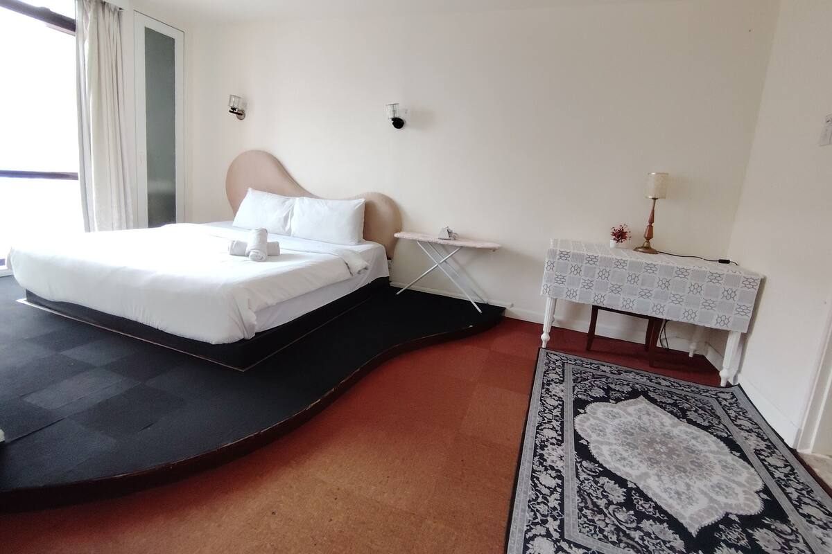 Una habitación de hotel con cama, una mesita de noche con lámpara y una alfombra estampada.