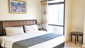 Ein Hotelzimmer mit einem großen Bett, einem Nachttisch, einem kleinen Tisch, einem Fenster mit Vorhängen und einem Gemälde an der Wand.