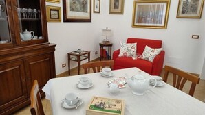A dining area with a table set for tea, a red sofa, and framed pictures on the wall. - Alcinque - Your home in Rome, in the heart of San Giovanni (Roma)
