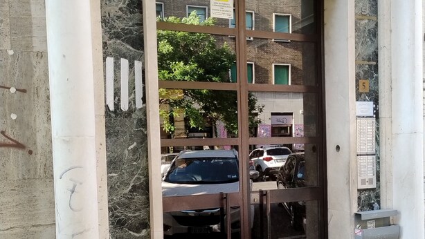 A building entrance with a glass door, a mailbox, and a number '5' sign. - Alcinque - Your home in Rome, in the heart of San Giovanni (Roma)