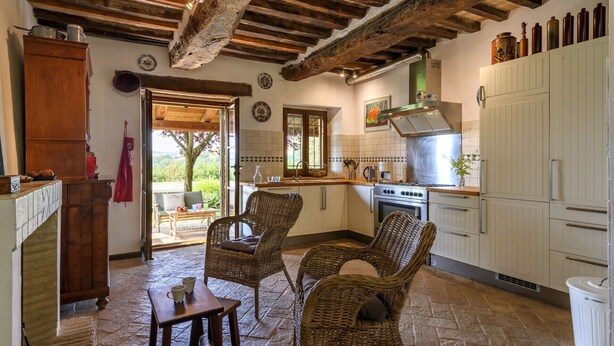 Una cocina rústica con vigas de madera a la vista, un ventanal grande y sillas de mimbre.