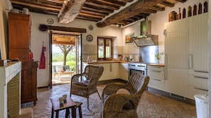A rustic kitchen with exposed wooden beams, a large window, and wicker chairs. - Ca Lucciola 12 by Marche Holiday Villas (Mondavio)