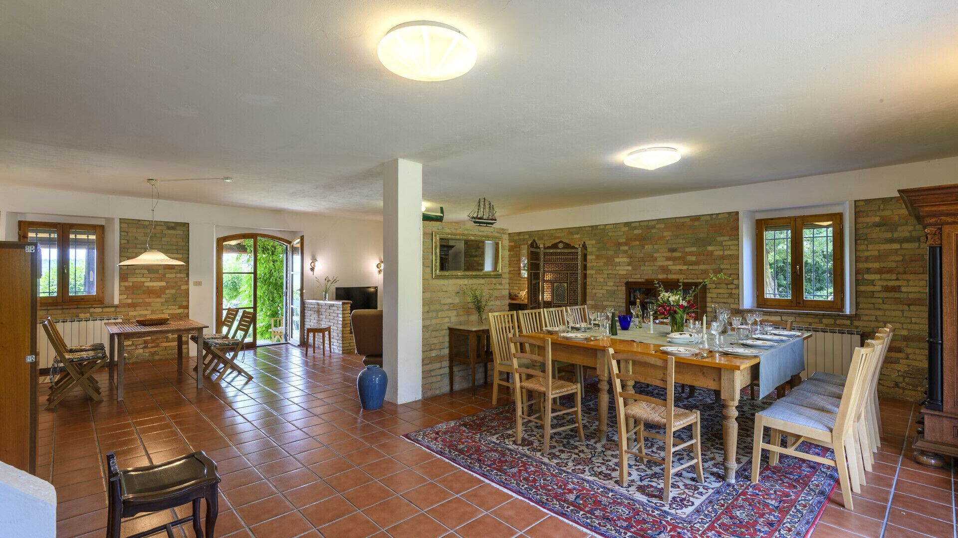 Un comedor amplio con una larga mesa de madera dispuesta para seis personas, rodeada de sillas. Una ventana grande ofrece luz natural y vistas al follaje exterior.
