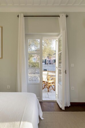 A bedroom with a bed, a window with white curtains, and a view of an outdoor patio area. - Daphne - Eight Bedroom Villa, Sleeps 16 (Agii Anargiri)