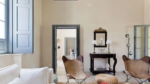 A living room with a white sofa, two leather chairs, a small table with a lamp, and a mirror.